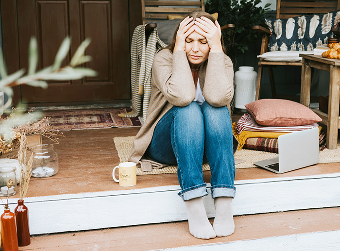 Woman sitting on porch steps looking stressed after business failure, refusing to get a job or have a boss.