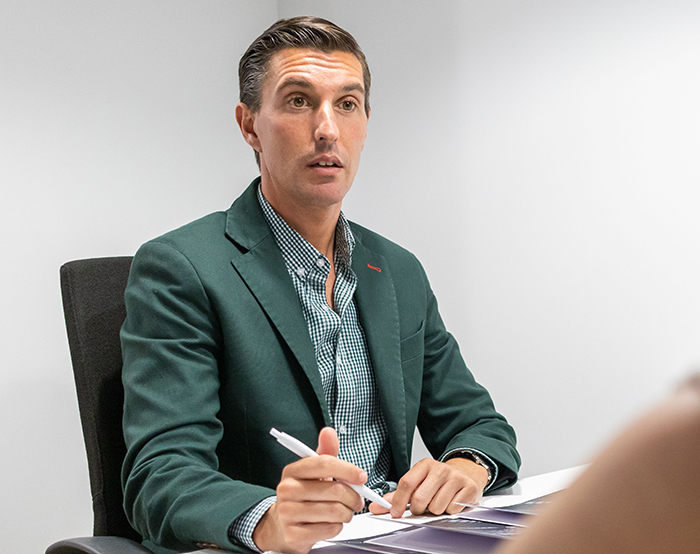 Man in a green jacket holding a pen during a serious discussion, illustrating a worker who goes above and beyond.