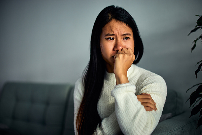 Woman looking worried and upset while sitting on a couch, reflecting on a man announces breakup to everyone except his girlfriend.