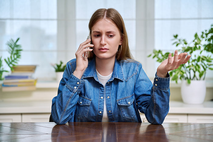 Young woman in denim jacket looking frustrated while talking on phone, defending aesthetic and social exclusion decisions.