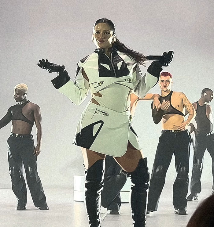Pop star modeling at Paris Fashion Week wearing a futuristic outfit with dancers, highlighting armpit hair dyed fashion trend.