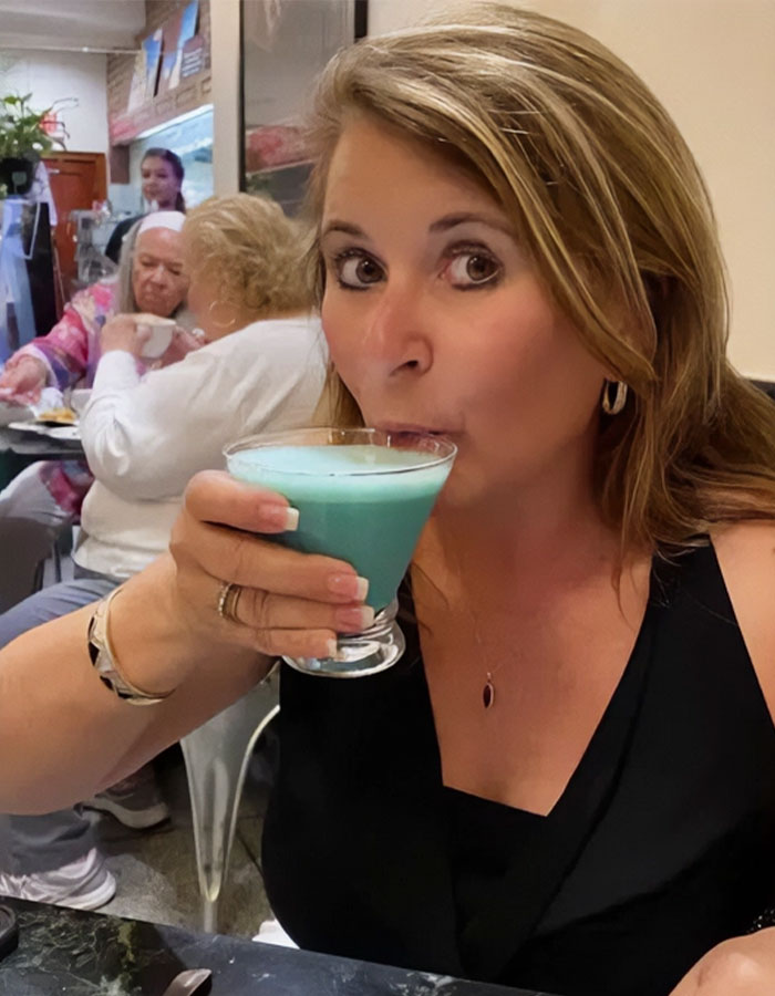 Woman enjoying a drink in a restaurant, relating to the story about a woman writing her own obituary humorously.