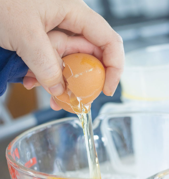 Person cracking an egg into a bowl, an example of people being shockingly unaware of common knowledge.