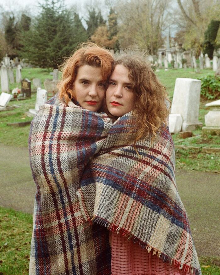 Two twins wrapped in a plaid blanket, captured by a London photographer highlighting their unique bond in portraits.