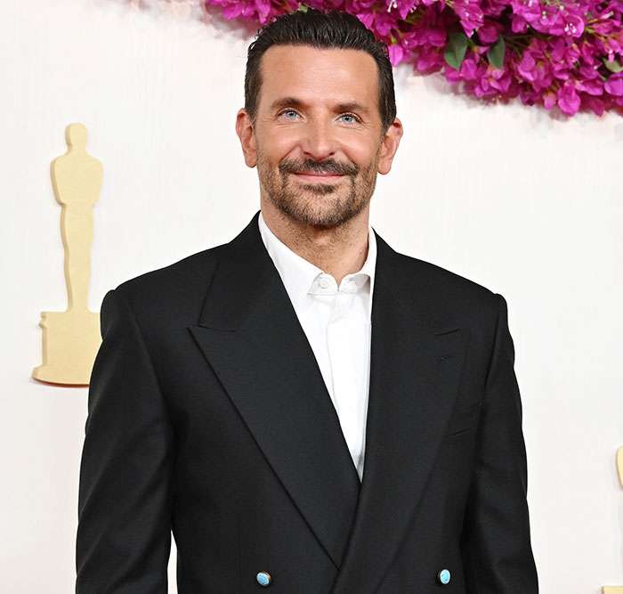 Bradley Cooper smiling in a black suit, with plastic surgeons commenting on his seemingly new look at an event. Bradley Cooper smiling in a black suit, with plastic surgeons commenting on his seemingly new look at an event.