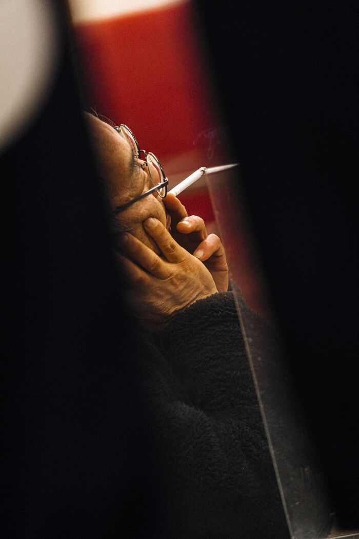 Close-up street photography shot of a person wearing glasses smoking a cigarette capturing life’s unexpected moments.