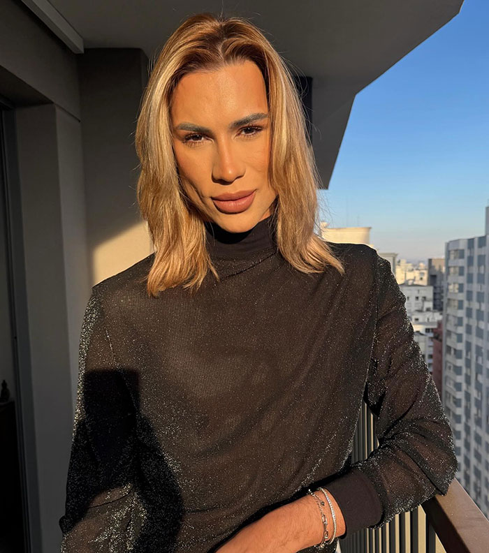 Influencer with blond hair wearing black top, posing on balcony, highlighting complications from popular fox eyes surgery.