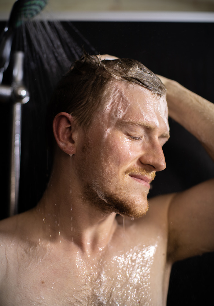 Man washing hair in shower, water flowing down, capturing a moment of unexpected and awkward times people saw something