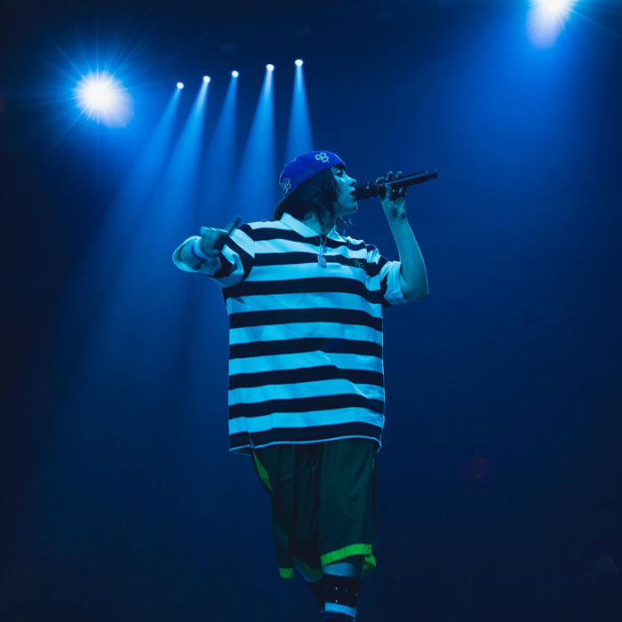 Billie Eilish performing on stage under blue lights during Miami concert with fans reacting to snatching attempt.