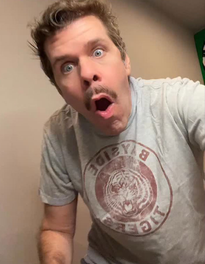 Man with a surprised expression wearing a gray t-shirt in a casual indoor setting, related to Bruce Willis' daughter and Perez Hilton. Man with a surprised expression wearing a gray t-shirt in a casual indoor setting, related to Bruce Willis' daughter and Perez Hilton.