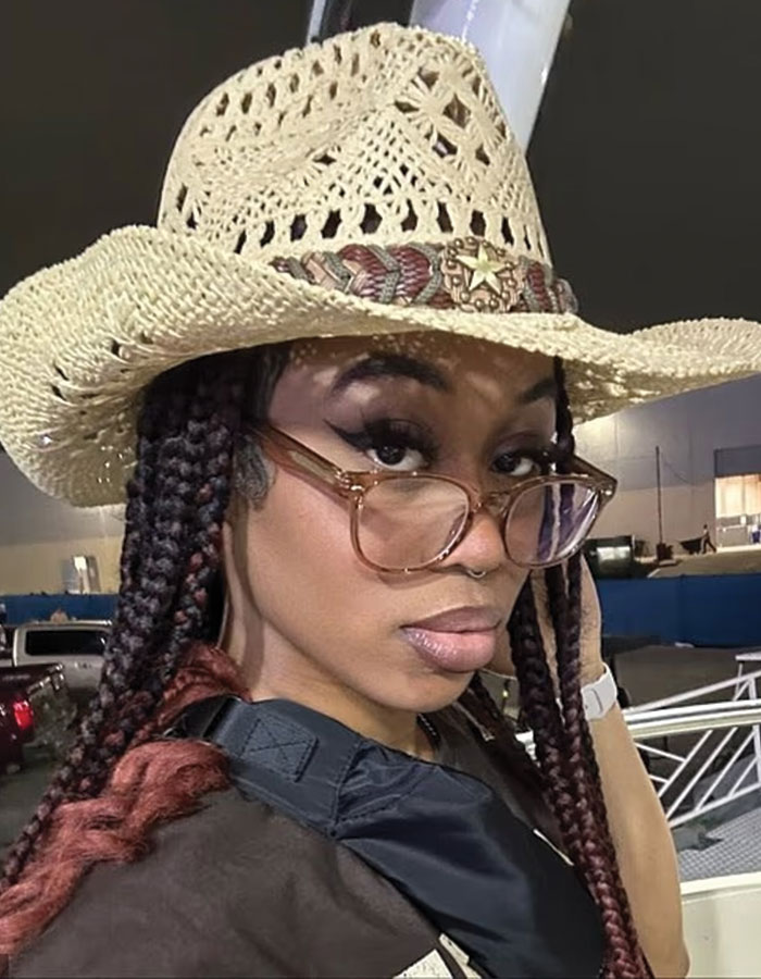Young woman with braided hair wearing a cowboy hat and glasses, outdoors at night in Houston city.