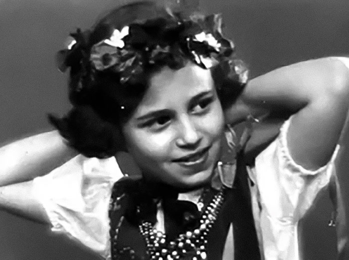 Black and white photo of Holocaust survivor Ruth Posner as a young girl wearing a floral headband and traditional clothing.
