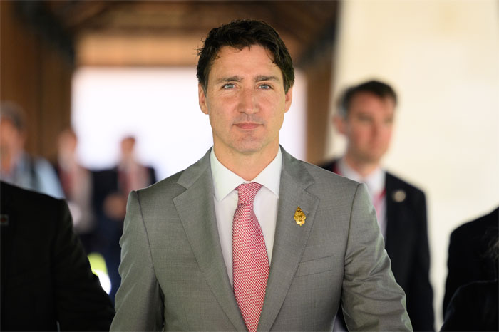 Justin Trudeau in a gray suit and pink tie, appearing serious as insiders brand his romance with Katy Perry a midlife crisis.