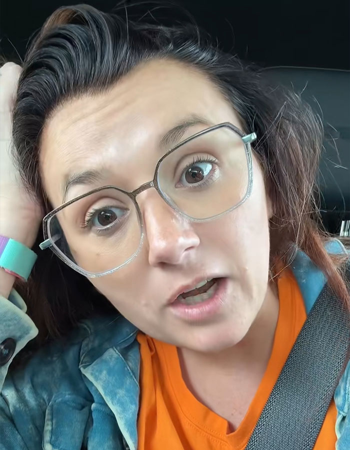 Woman with glasses and orange shirt expressing shock and anger, reacting to husband&rsquo;s infidelity during mid-flight confrontation