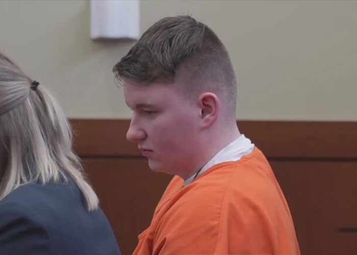 Young man in orange prison uniform sitting in courtroom during legal proceedings related to newborn baby case.