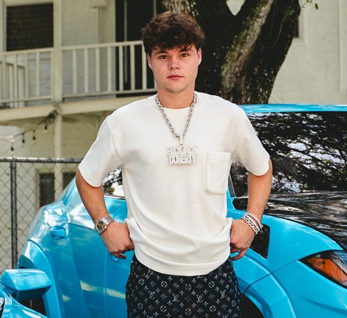 Young man standing confidently by a blue car, highlighting disturbing new details after adult star split from YouTube prankster.