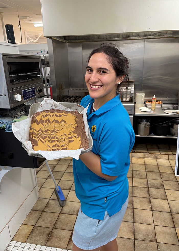 Woman smiling in kitchen holding tray with patterned dessert, related to insurance company denied coverage over bird incident.