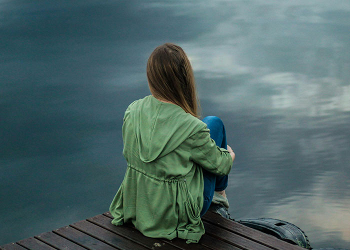 Person in a green jacket sitting alone on a dock by calm water reflecting the cloudy sky, illustrating mental health myths.