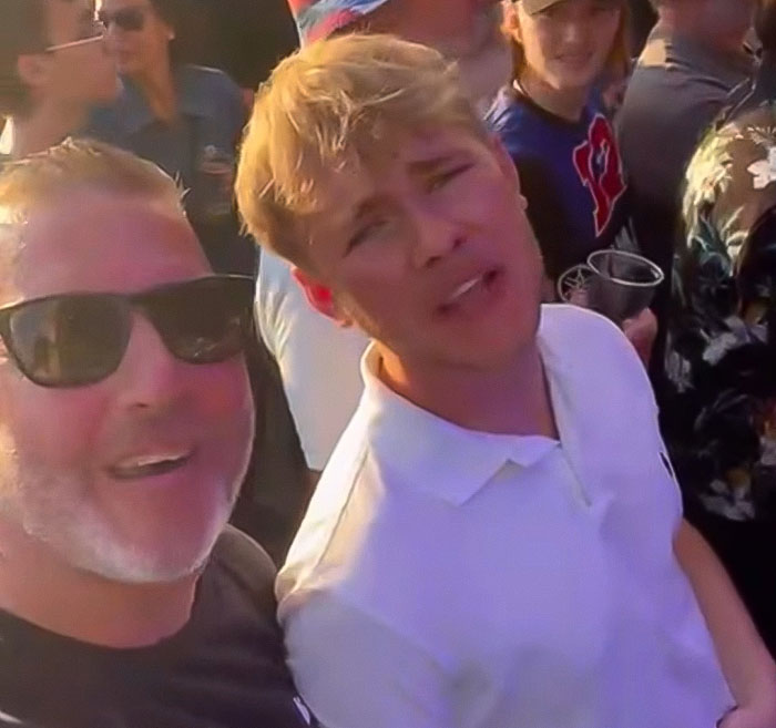 Two men at a crowded rock concert, one wearing sunglasses, capturing a moment before a leg amputation decision.