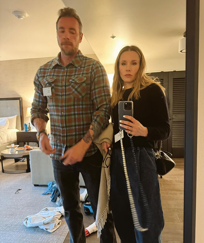 Kristen Bell taking a mirror selfie with a man in a casual room, amid experts condemning her triggering post and behavior.