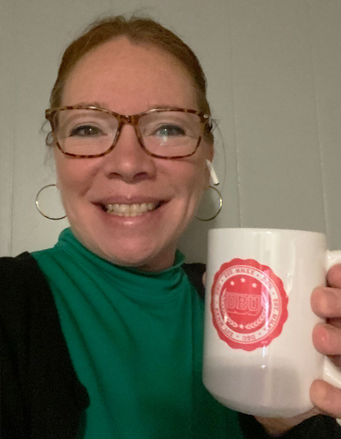 Female Teacher of the Year finalist wearing glasses and holding a white mug, smiling in an indoor setting.