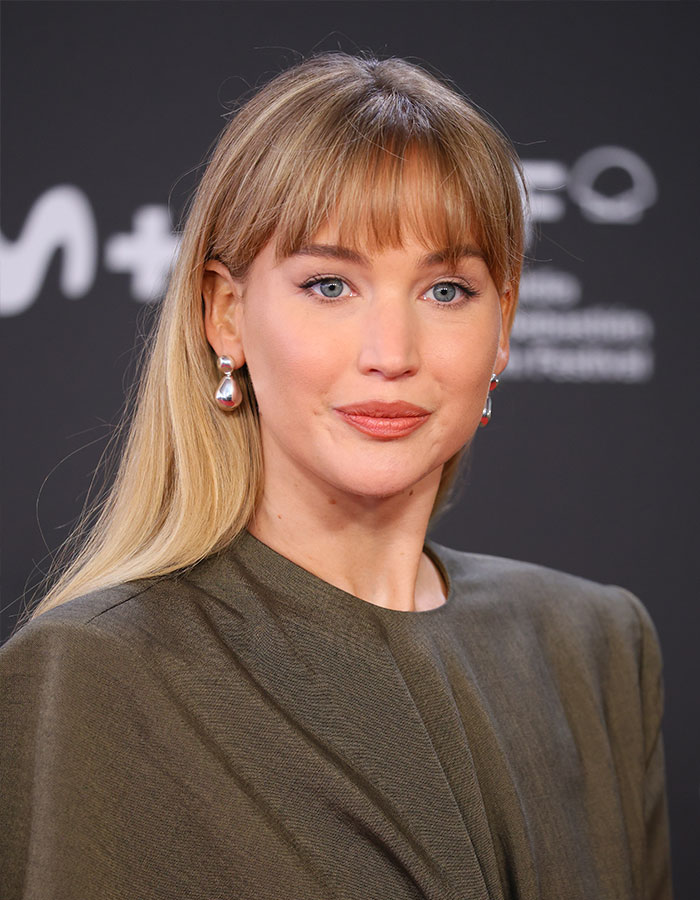Jennifer Lawrence at an event, wearing earrings and a dark outfit, addressing plastic surgery plans after viral fan reactions.