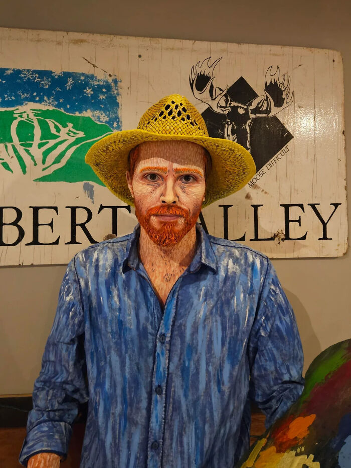 Artist with hand-painted makeup and costume transforming into Vincent van Gogh wearing a yellow hat and blue shirt.