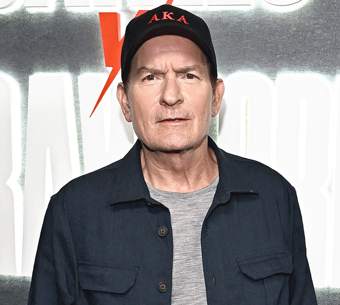 Emilio Estevez wearing a cap and jacket posing in front of a backdrop featuring movie graphics and logos Emilio Estevez wearing a cap and jacket posing in front of a backdrop featuring movie graphics and logos