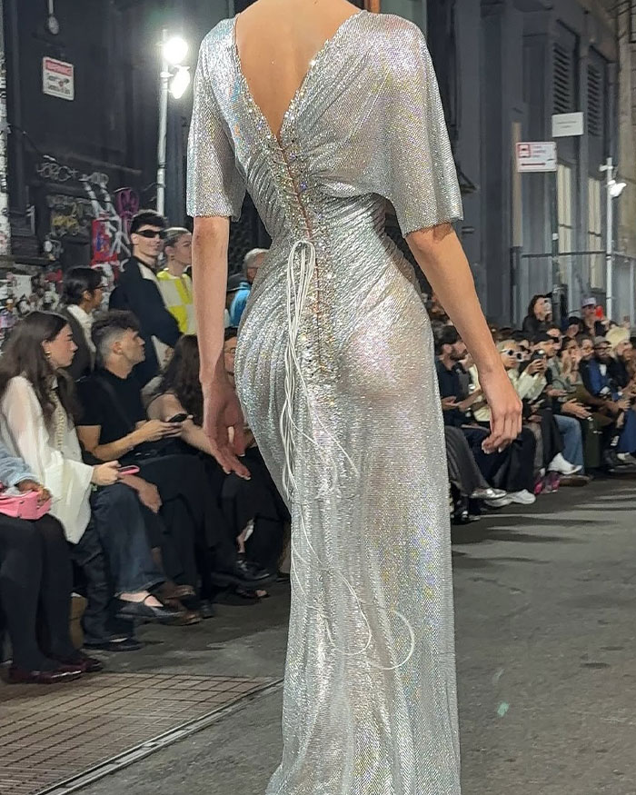Model wearing a shimmering silver gown with intricate back lace-up details, showcasing Sydney Sweeney&rsquo;s gravity-defying dress design.