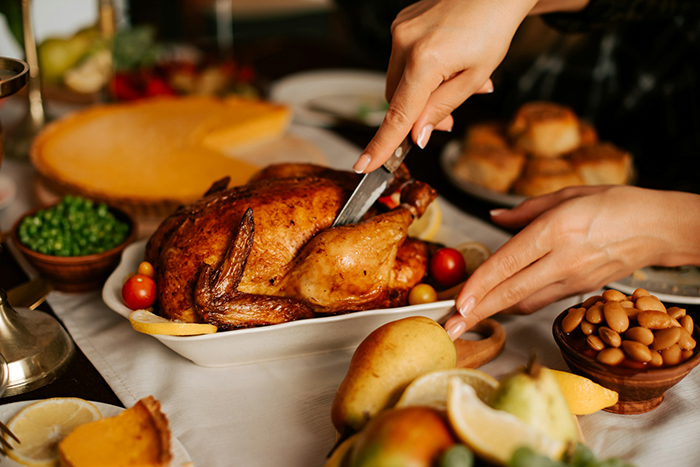 Woman carving Thanksgiving turkey at festive table with classic side dishes in warm holiday setting