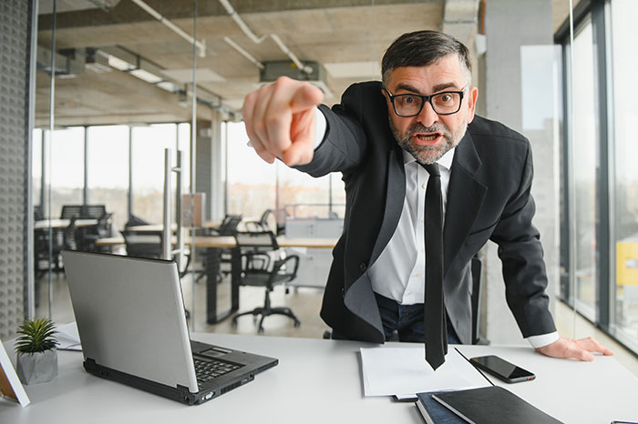 Angry boss pointing aggressively at employee in office, upset they didn&rsquo;t check email on their way to work.