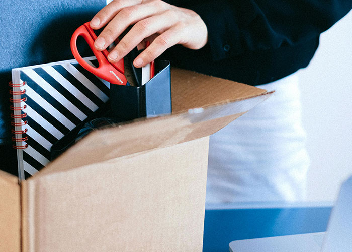 Person packing office supplies into a box, illustrating creative loopholes against horrible bosses in the workplace.