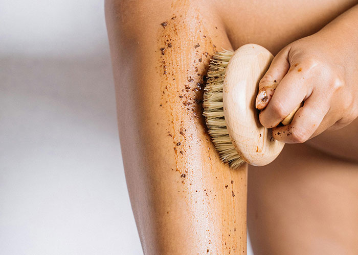 Person exfoliating leg with a dry brush and scrub, illustrating self-care before cosmetic procedure decisions.
