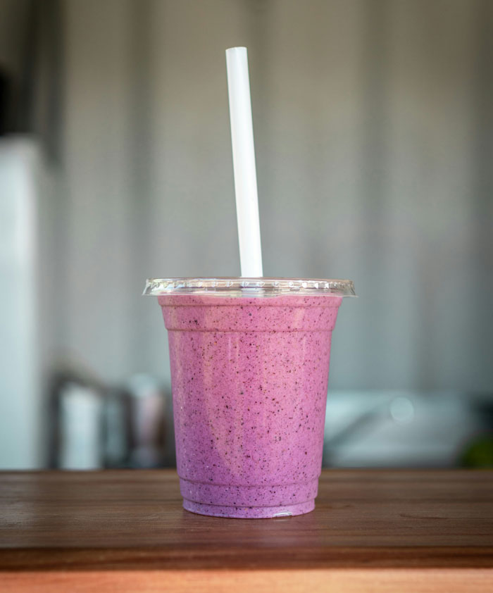 Purple smoothie in a clear plastic cup with a white straw on a wooden table, symbolizing worst employees stories.