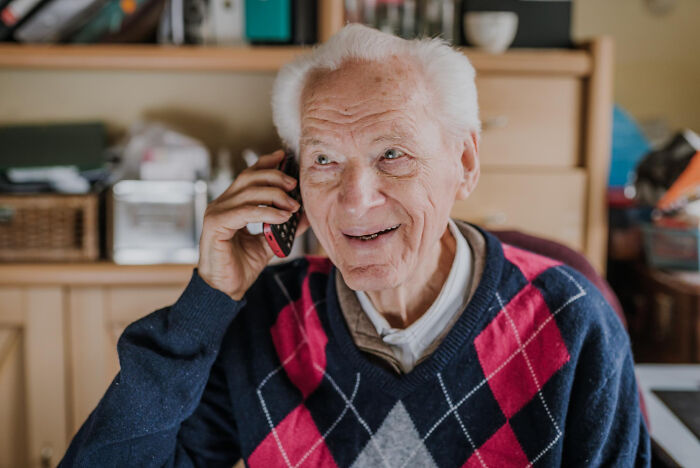 Elderly man with bad technology skills laughing while talking on a mobile phone, capturing a funny moment.