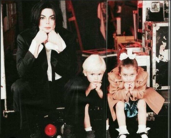 Michael Jackson with children Paris Jackson and Blanket, highlighting family and estate tensions in a posed backstage setting.
