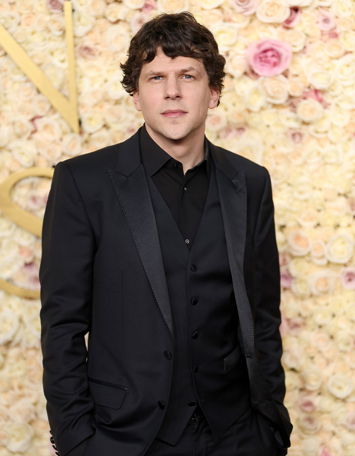 Actor wearing a black suit posing against a floral backdrop, representing famous men who are much shorter than fans imagined.