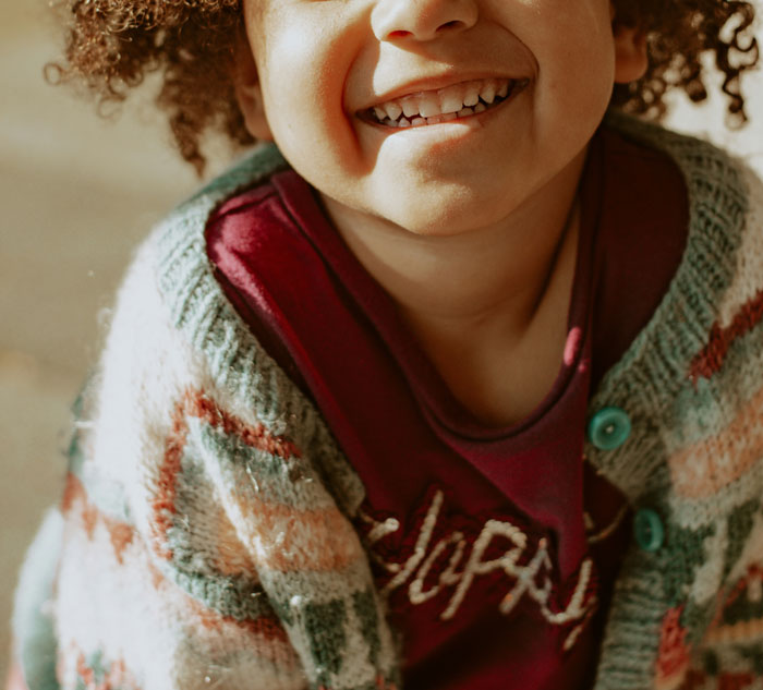 Smiling young child wearing a colorful knit sweater, representing daycare workers hearing unexpected family secrets.