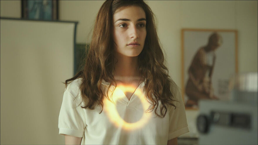 Young woman in a white shirt with a glowing ring reflection, representing movies based on true stories that feel impossible to believe.