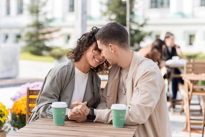 Couple holding hands and leaning close at a café, illustrating social cues in a hilariously painful moment outdoors.