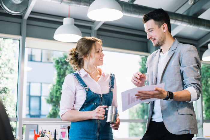 Two coworkers discussing documents in a modern office, highlighting highly disturbing things people only later realized were creepy.