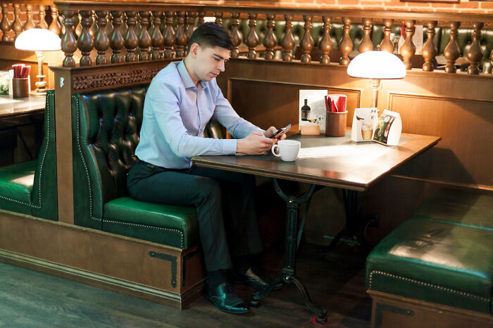 Man in a restaurant booth checking his phone with a coffee cup, illustrating restaurant staff stories about unpaid bills.