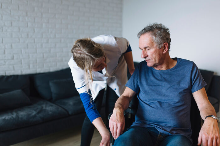 Caregiver assisting an elderly man with dementia in a wheelchair in a cozy living room setting.