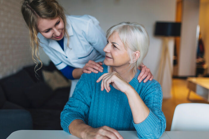 A caregiver gently supporting a senior woman with dementia, sharing a warm moment in a cozy home setting.
