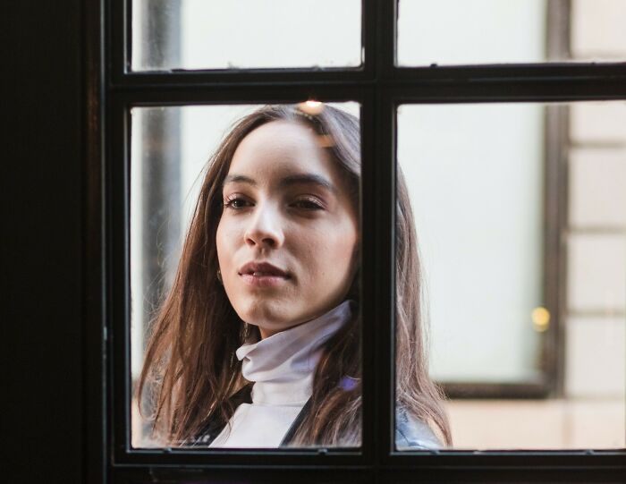 Young woman looking thoughtfully through a window, illustrating intense stalking behavior discussed by women in FBI-related stories.