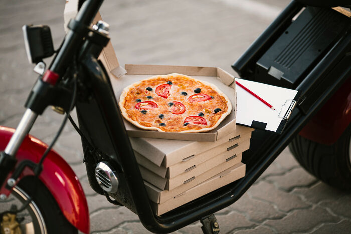 Stack of pizza delivery boxes with a fresh pizza and receipt on a scooter, illustrating restaurant staff billing and payment issues.