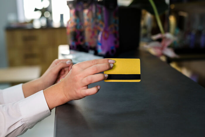 Hands of a restaurant customer holding a yellow credit card over the counter representing bill payment issues at restaurants