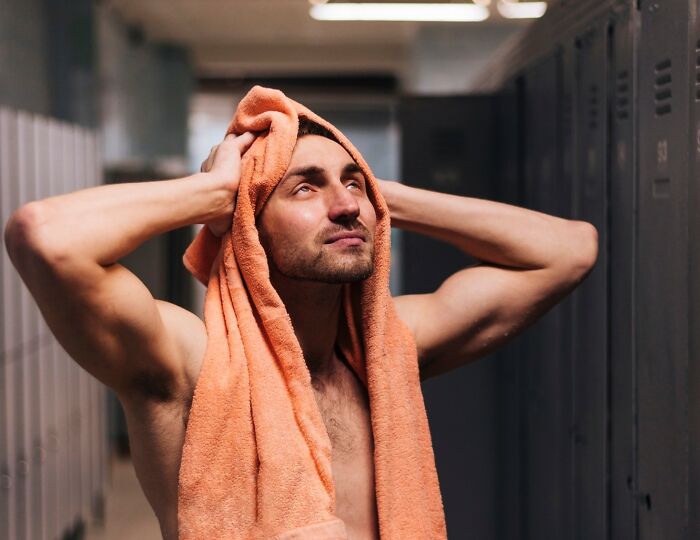 Man in a locker room with a towel on his head, looking up thoughtfully after a workout or shower session.