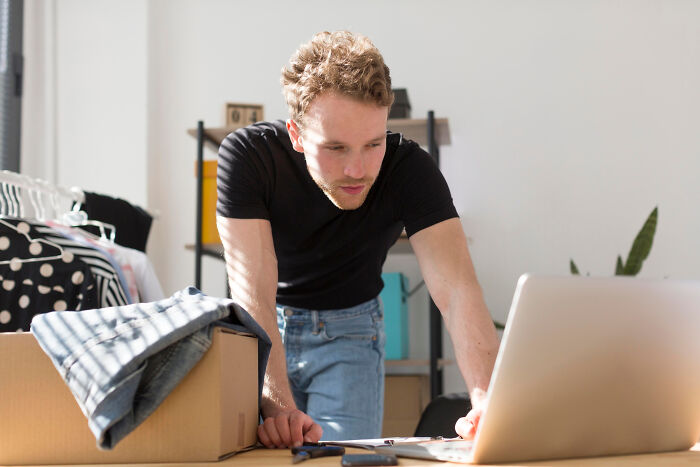 Man leaning over table with moving boxes, using a laptop to plan how to zip-line your boxes out efficiently.