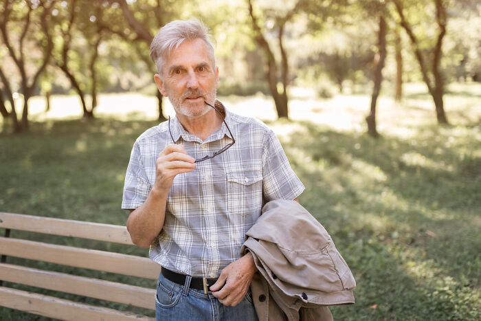 Older man in a plaid shirt holding glasses and jacket, reflecting on highly disturbing things people were told that seem creepy.